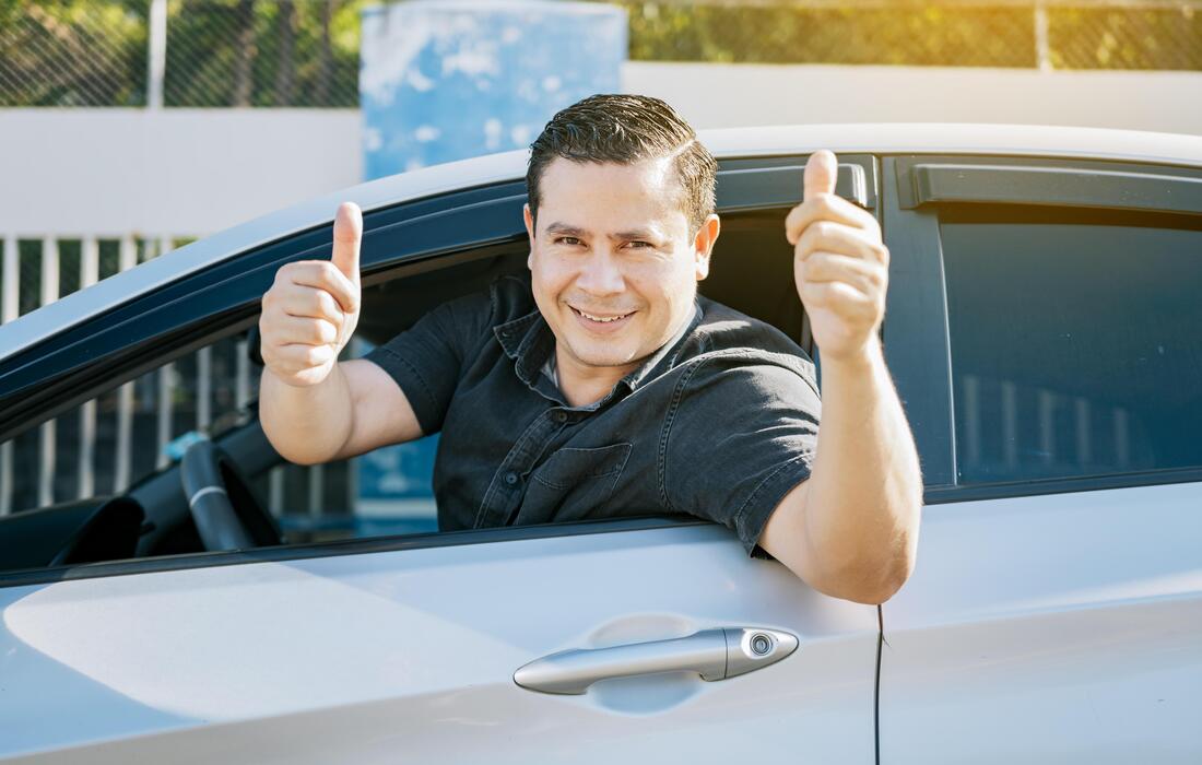 A smiling driver holding a car key and showing a thumbs up, representing successful insurance savings